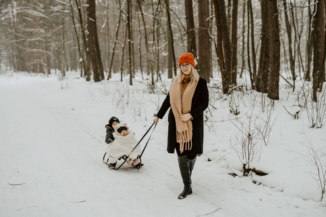 zdjęcie z sesji rodzinnej mamy ciągnącej synka na sankach w lesie pod Warszawą