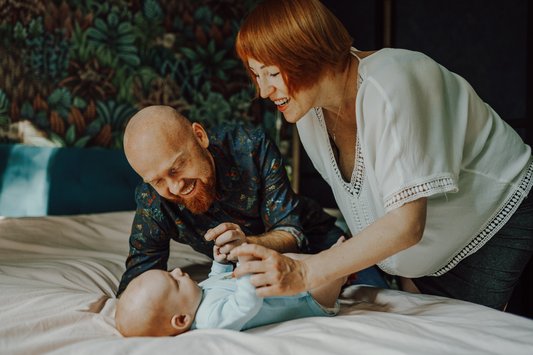 rodzice bawiący się z niemowlakiem na łóżku podczas sesji noworodkowej