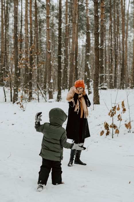 fotografia dziecka rzucającego w mamę śnieżką podczas sesji zimowej w lesie pod Warszawą