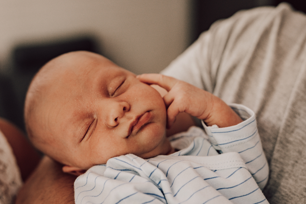 śpiący noworodek trzymający palec pod brodą poczas sesji noworodkowej