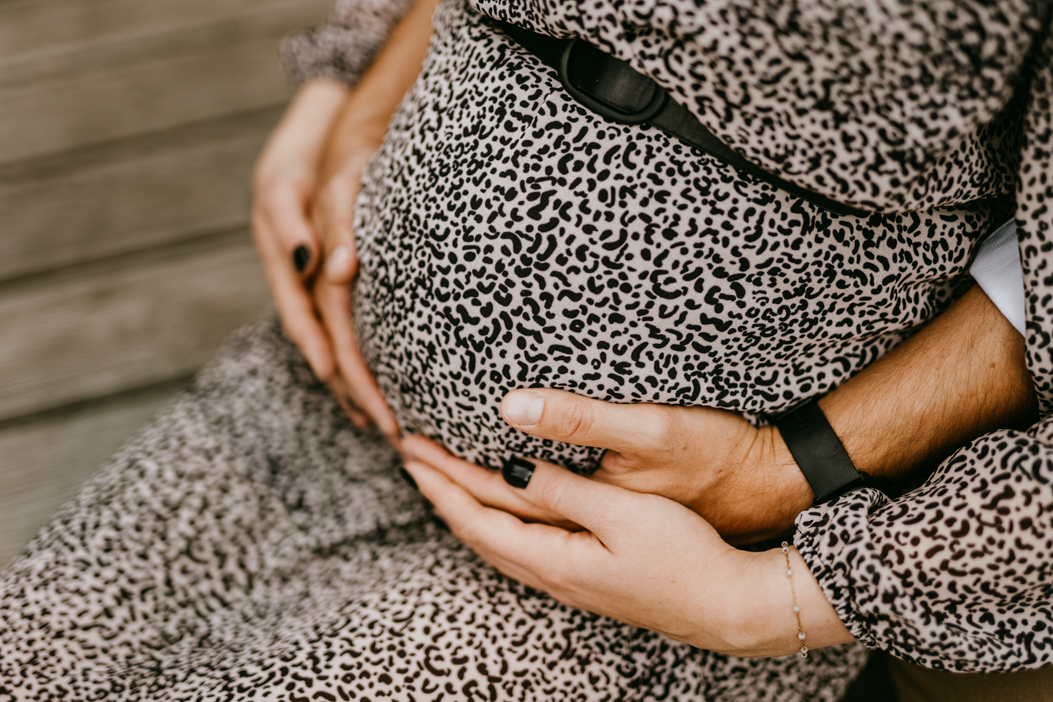fotografia brzuszka ciążowego, oplecionego dłoniami pary spodziewającej się dziecka