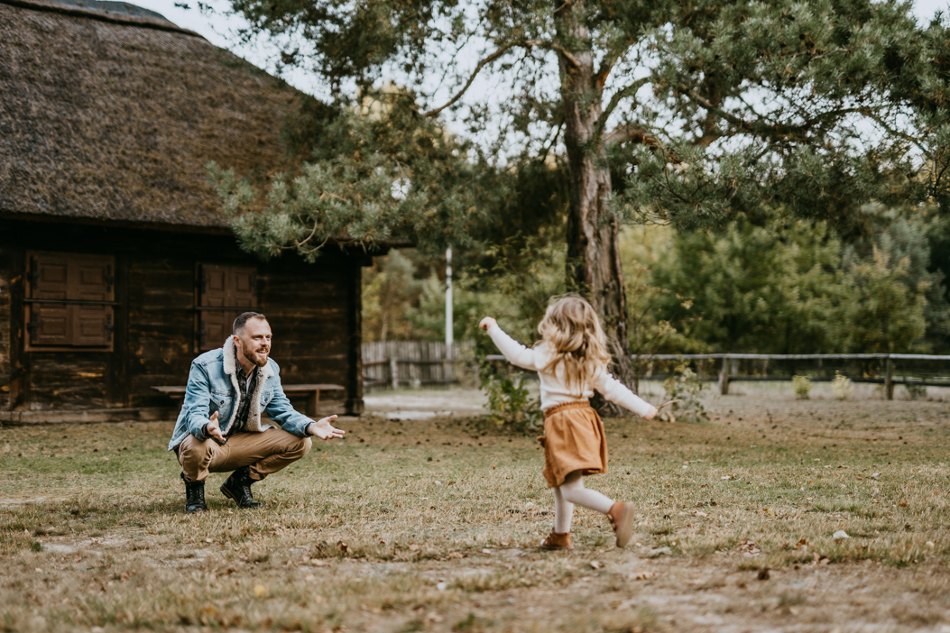blondwłosa dziewczynka  w spódniczce biegnąca do taty podczas sesji rodzinnej w plenerze
