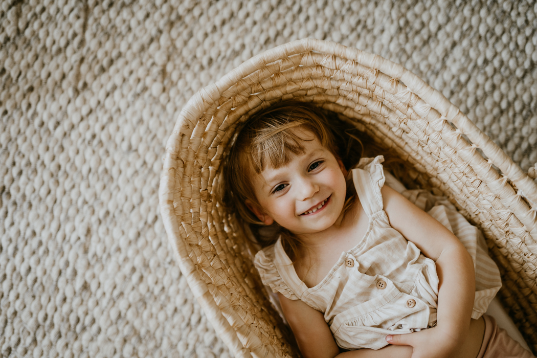 dwuletnia dziewczynka w blon włosach i jasnej sukience leżąca w koszu mojżesza