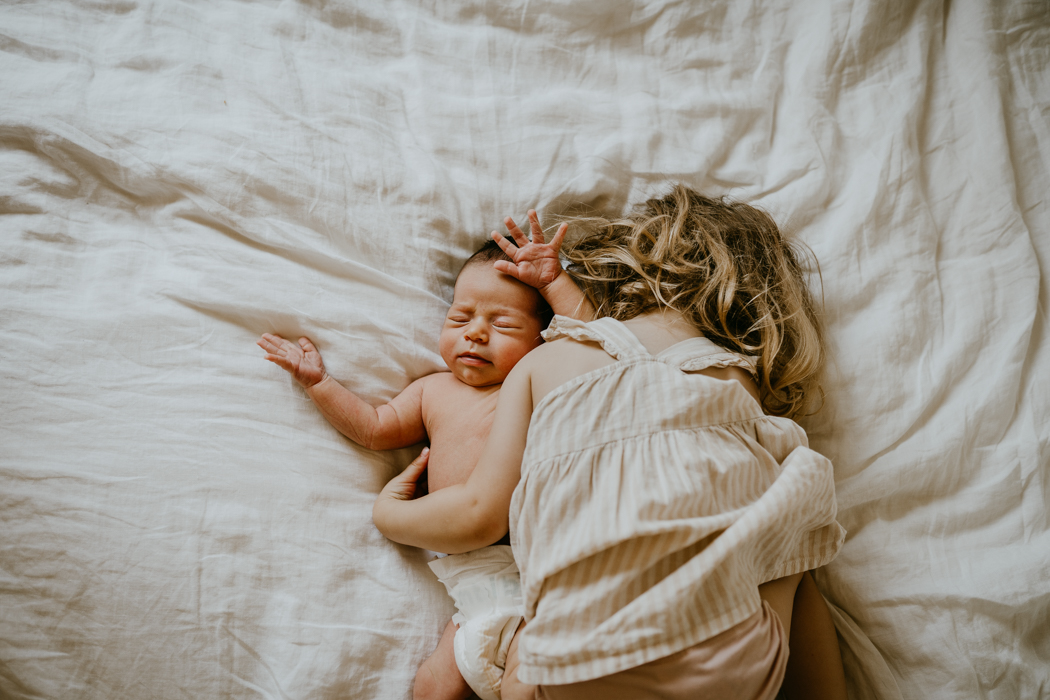 noworodek ubrany w samego pampersa leżący na łóżku ze swoją starszą siostrą na domowej sesji lifestyle w warszawie