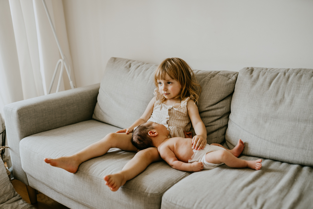 zdjecie noworodka, którego na kolanach trzyma dwuletnia siostra podczas domowej sesji lifestyle w Warszawie