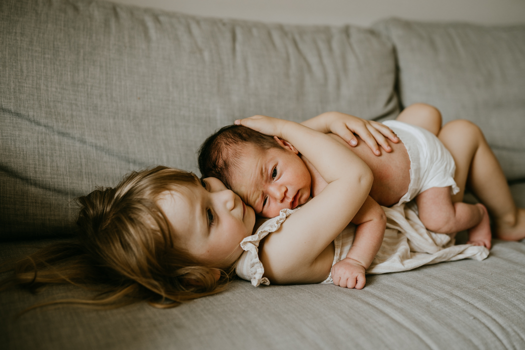 starsza siostra przytulajaca noworodka na domowej sesji zdjęciowej