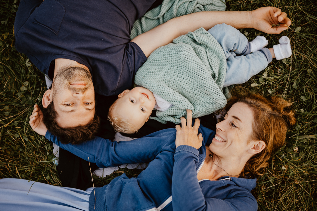 rodzinne zdjęcie mamy, taty i małego chłopca, którzy leżą na trawie podczas sesji rodzinnej w Warszawie