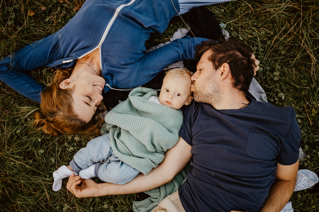 rodzinne  zdjęcie rudej mamy, taty i blond chłopca, którzy leżą na trawie podczas sesji niemowlęcej w Warszawie