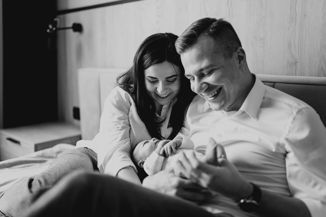 czarno-biała forografia szczęśliwych świeżoupiecznych rodziców trzymających na rękach noworodka