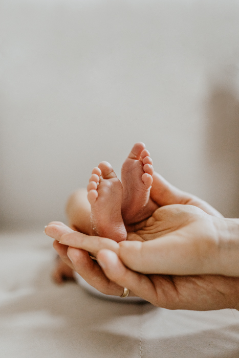 zdjęcie stópek noworodka które są podtrzymywane dłońmi rodziców
