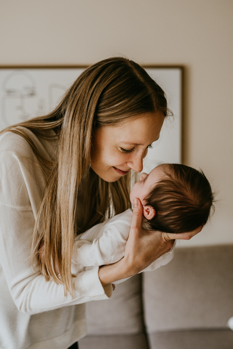 młoda mama trzymająca dziecko i pocierająca jego nosek swoim nosem na naturalnej sesji noworodkowej w domu w warszawie