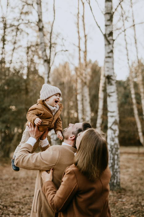 szczęśliwi rodzice podrzucający dziecko do góry na jesiennej sesji pod Warszawą