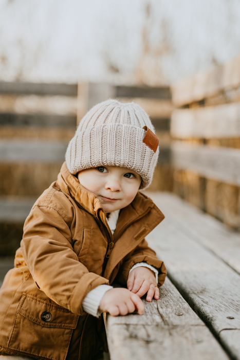 zdjęcie rocznego chłopca w brązowej kurtce i beżowej czapce opierający się o ławkę