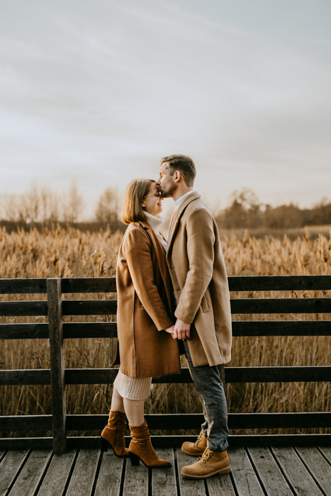romantyczne zdjęcie małżeństwa trzymającego się za ręce na drewnianym pomoście na tle traw pampasowych