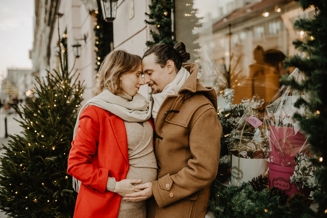romantyczne zdjęcie pary w ciąży na tle choinek i świątecznej witryny sklepowej