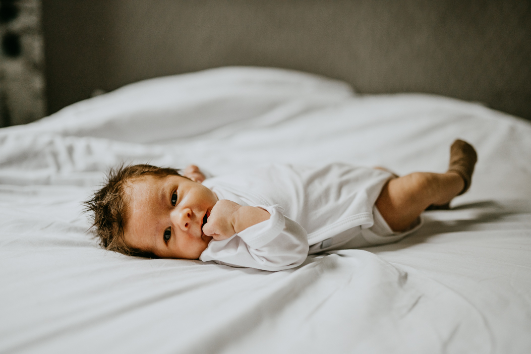 noworodek z długimi ciemnymi włosami leżący na łóżku w białej pościeli