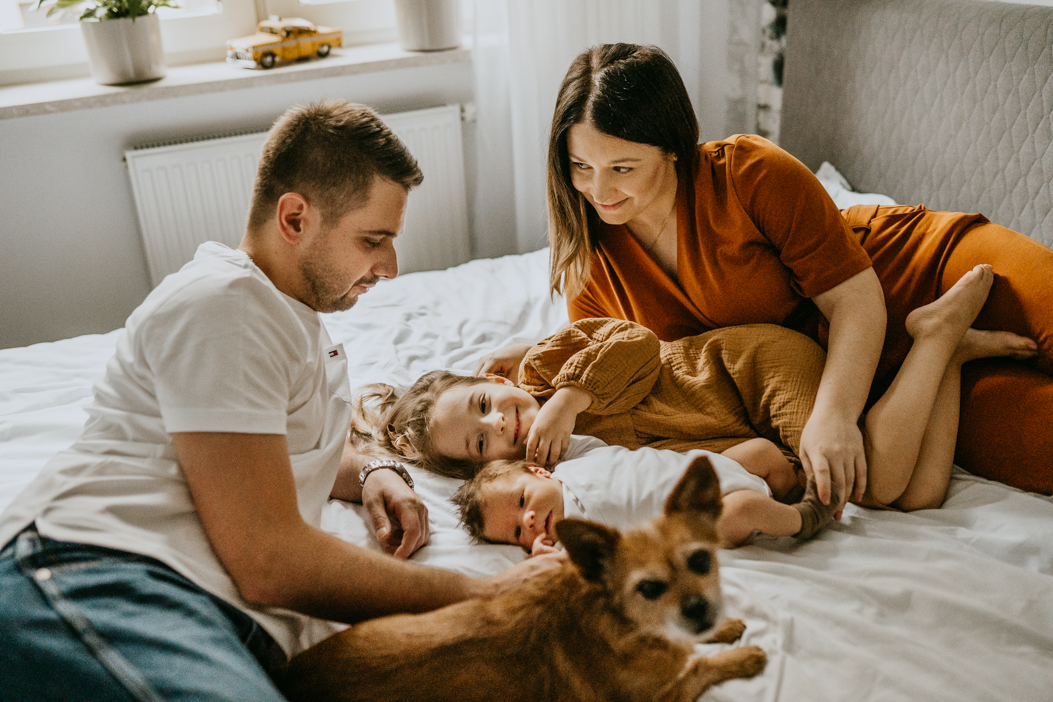 naturalna fotografia rodziny leżącej na łóżku z małym rudym psem podczas sesji lifestyle w Warszawie