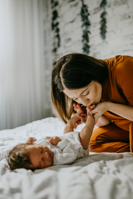śliczna mama całująca stópki noworodka podczas naturalnej sesji noworodkowej wykonanej przez fotografa rodzinnego z Warszawy