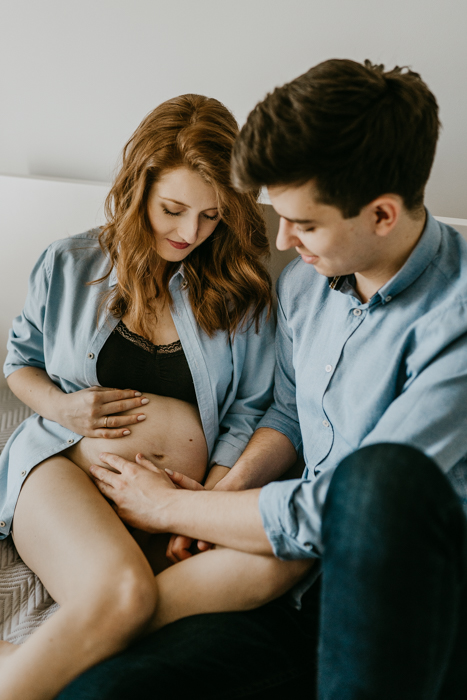 przyszli rodzice przyglądający się i dotykający brzucha ciążowego podczas domowej sesji ciążowej