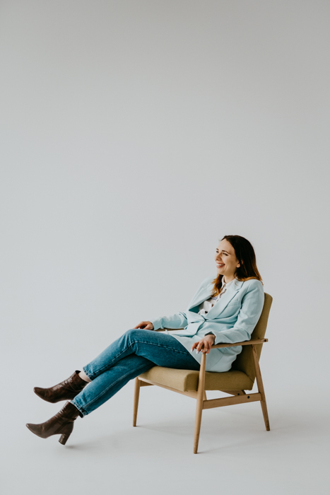 elegancko ubrana kobieta siedząca na fotelu na białym tle pozując do sesji wizerunkowej w studio