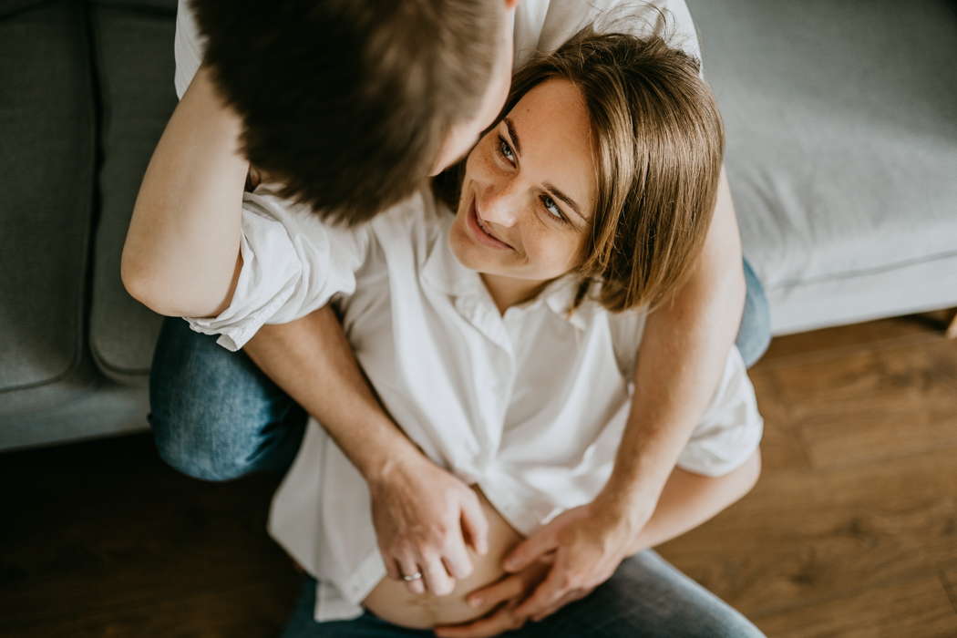 kobieta w ciąży przytulająca się z mężem podczas domowej sesji zdjęciowej