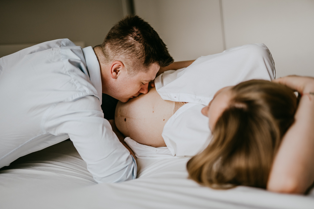 mężczyzna całujący brzuch ciążowy swojej partnerki podczas sesji zdjęciowej w domu w Warszawie