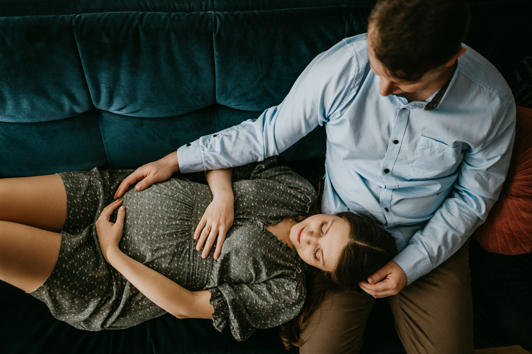 kobieta leżąca z partnerem na sofie i trzymajaca brzuszek ciążowy podczas domowej sesji u fotografa z warszawy