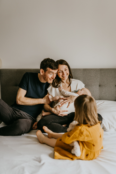 rodzice siedzący na łóżku z niemowlakiem i córeczką w żółtej sukience na domowej sesji w ich mieszkaniu w warszawie