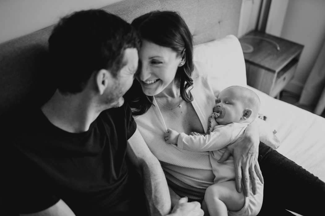 czarno-białe zdjęcie rodziców trzymajacych na rękach niemowlaka i patrzących sobie w oczy podczas naturalnej sesji rodzinnej w warszawie