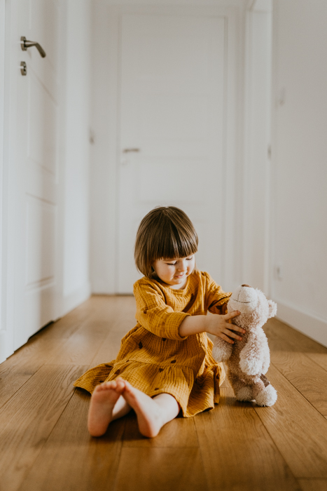 dziewczynka z grzywką bawiąca się na podłodze w korytarzu na naturalnej sesji rodzinnej w domu