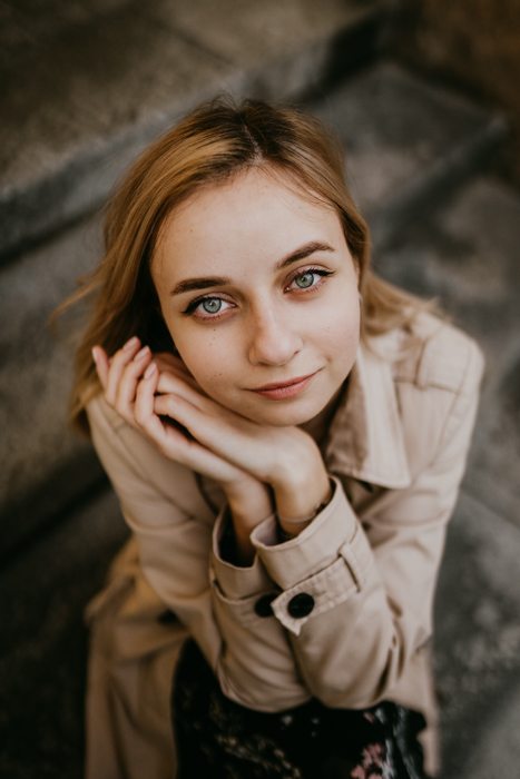 subtelne zdjęcie portretowe młodziej dziewczyny z blond włosami i zielonymi oczami siedzącej na schodach podczas sesji zdjciowej w centrum Warszawy