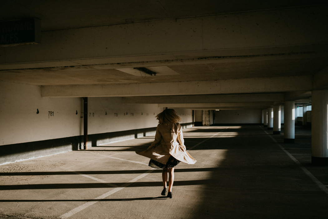 kobieta obracająca się w okół własnej osi na pustym parkingu piętrowym na ziemi którego tworzą się piękne światłocienie