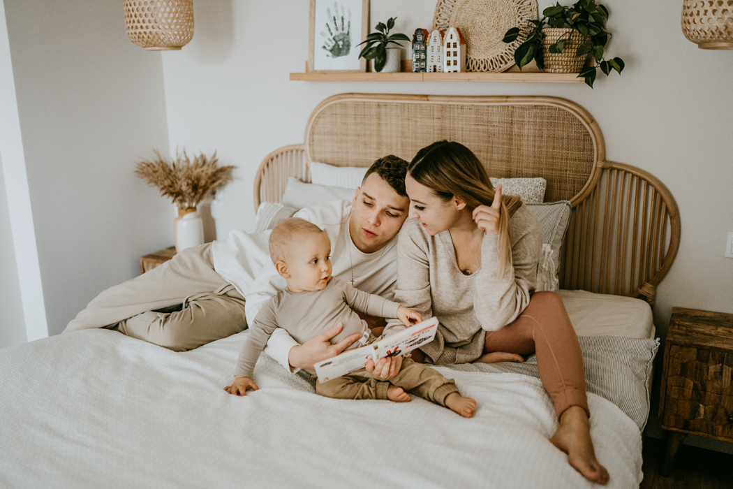 rodzinne zdjęcie w sypialni na białej pościeli trzyosobowej rodziny wykonane na sesji zdjęciowej z okazji pierwszych urodzin