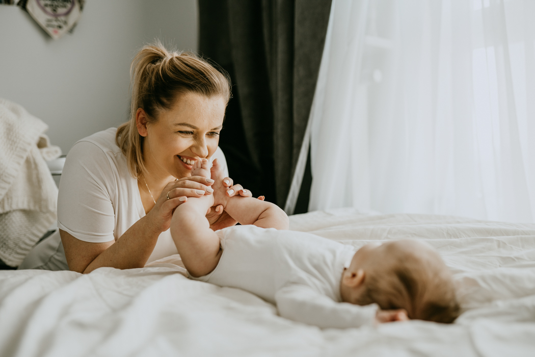 blondwłoda mama całująca stópki dzidziusiowi podczas naturalnej sesji niemowlęcej w Warszawie