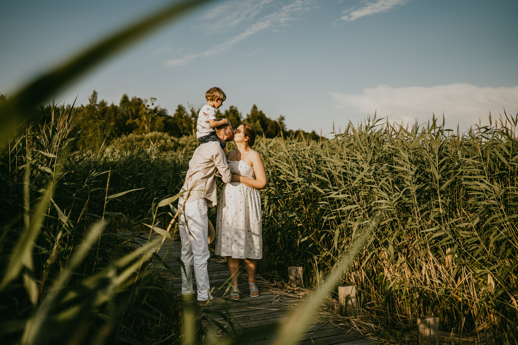 zdjęcie całujących się rodziców i dziecka wśród wysokich traw wykonane na sesji ciążowo-rodzinnej przez fotografa z Warszawy