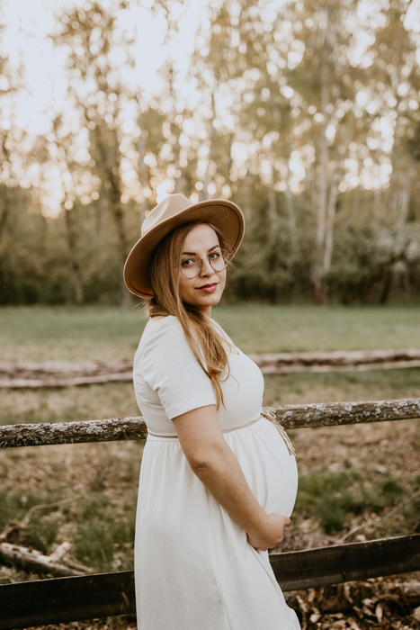 fotografia młodej kobiety w ciąży ubranej w kremową sukienkę z odcięciem pod biustem oraz w kapelusz 