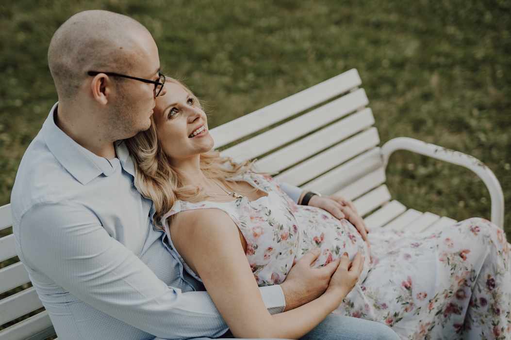 zdjęcie ciążowe pary obejmującej się na ławce i dotykającej brzucha w parku w warszawie