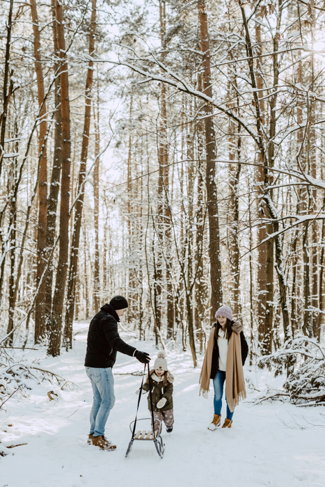 rodzice z dzieckiem i sankami podczas sesji zdjęciowej w śnieżnym lesie