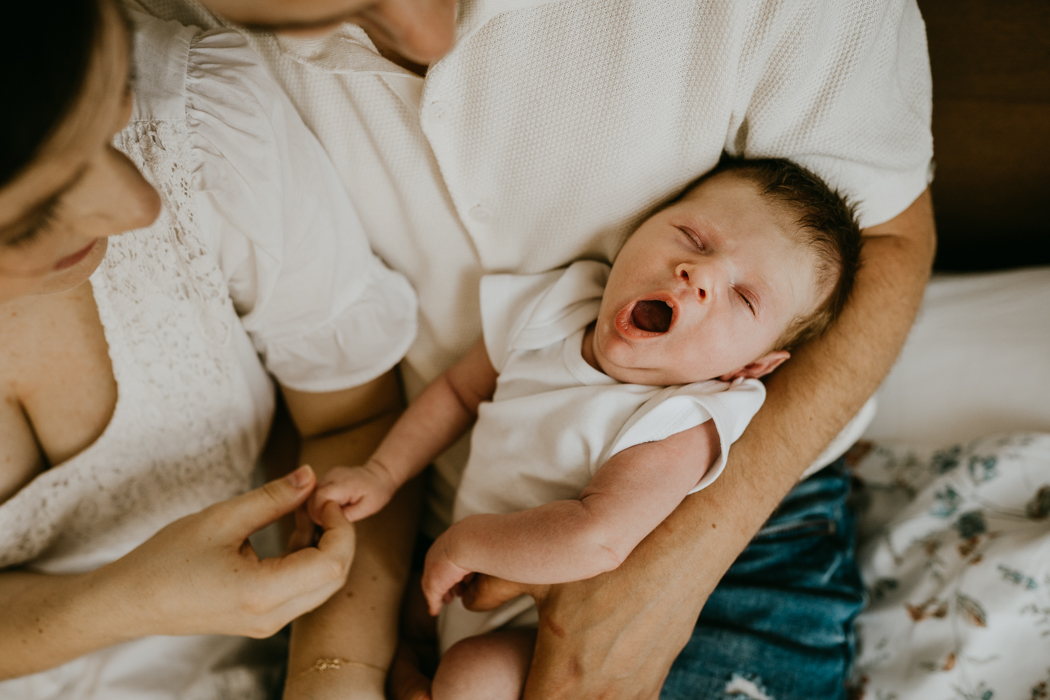 ziewający noworodek na rękach u rodziców uchwycony przez fotografa noworodkowego z warszawy