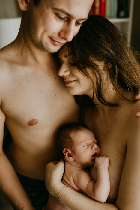 fotografia noworodka podczas kontaktu skóra do skóry z rodzicami podczas sesji noworodkowej w domu w warszawie