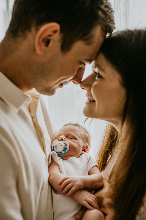 fotografia patrzących sobie w oczy rodziców trzymającyh na rękach noworodka wykonana podczas sesji w domu