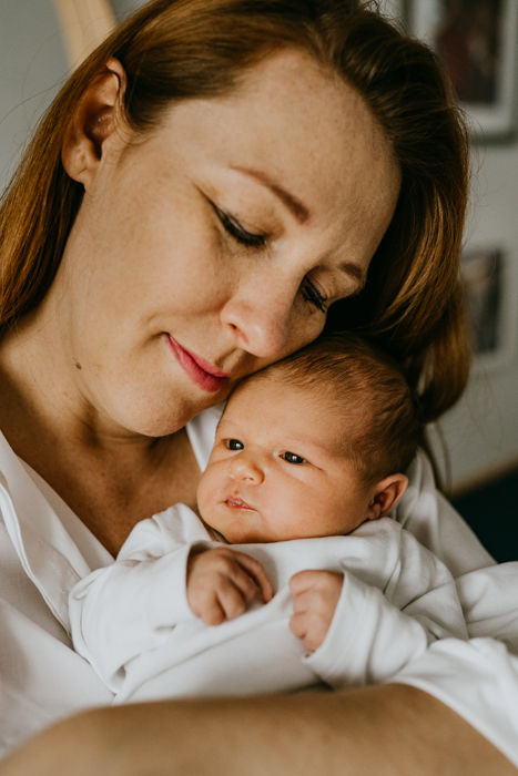 rudowłosa mama w białej koszuli trzymająca na rękach noworodka podczas sesji rodzinnej w domu w warszawie