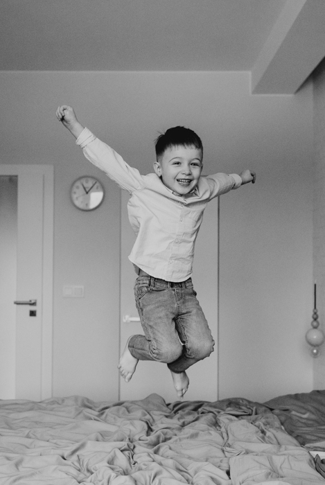 czarno-biała fotografia dziecka skaczącego na łóżku podczas sesji domowej